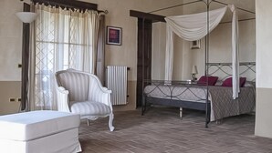 A bedroom with a four-poster bed, a chair, a bedside table, and a radiator. - Casale Farnia - Tenuta di campagna con piscina immersa nel verde (Montecastrilli)