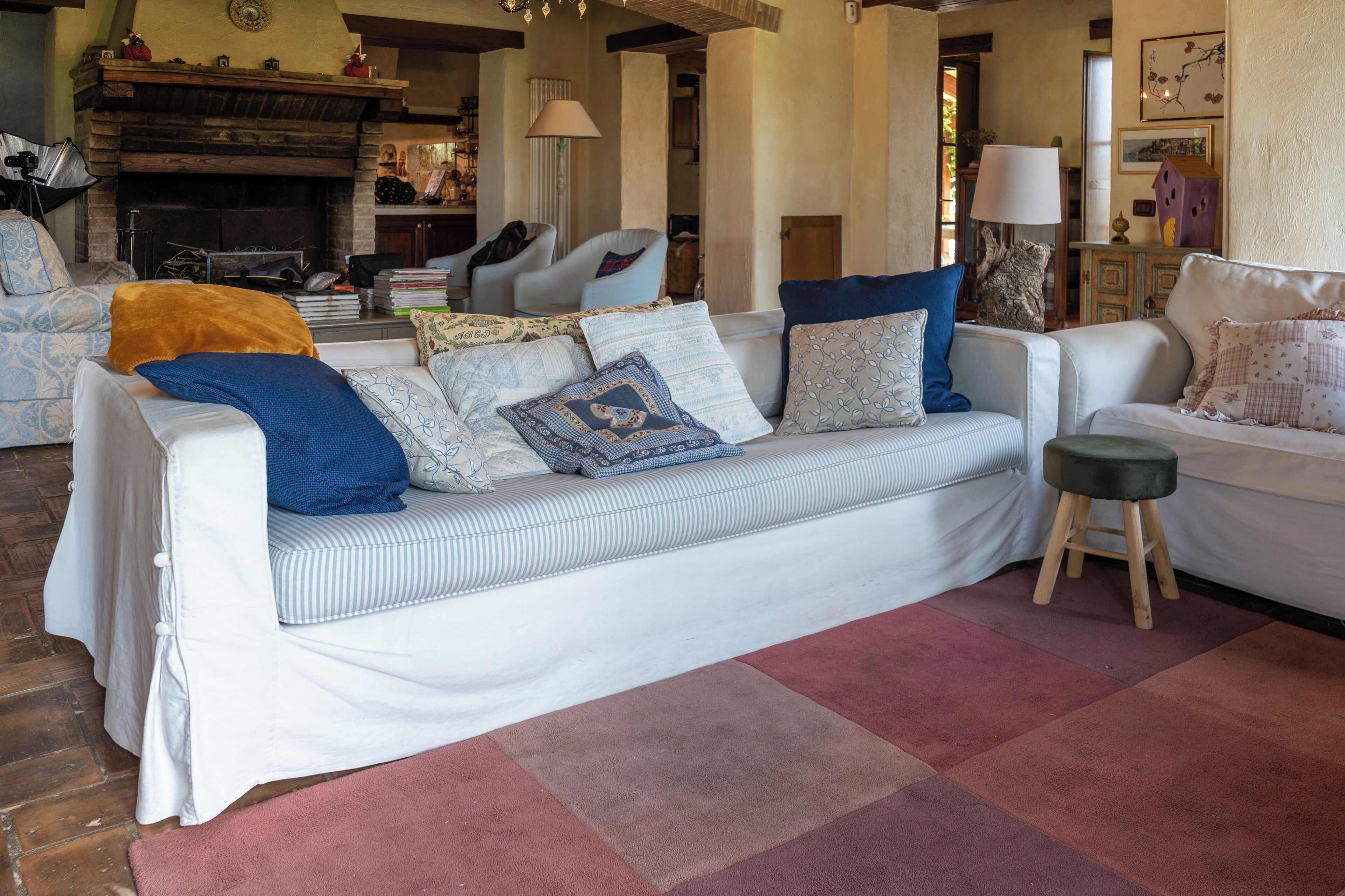 A cozy living room with a white sofa adorned with patterned cushions, a wooden floor, and a fireplace in the background.