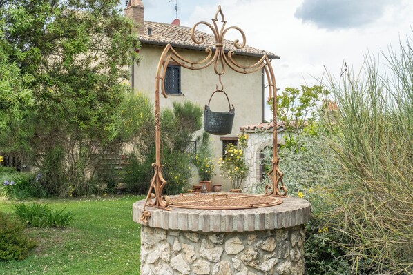 A rustic outdoor stone well with a metal bucket suspended by a decorative metal frame.