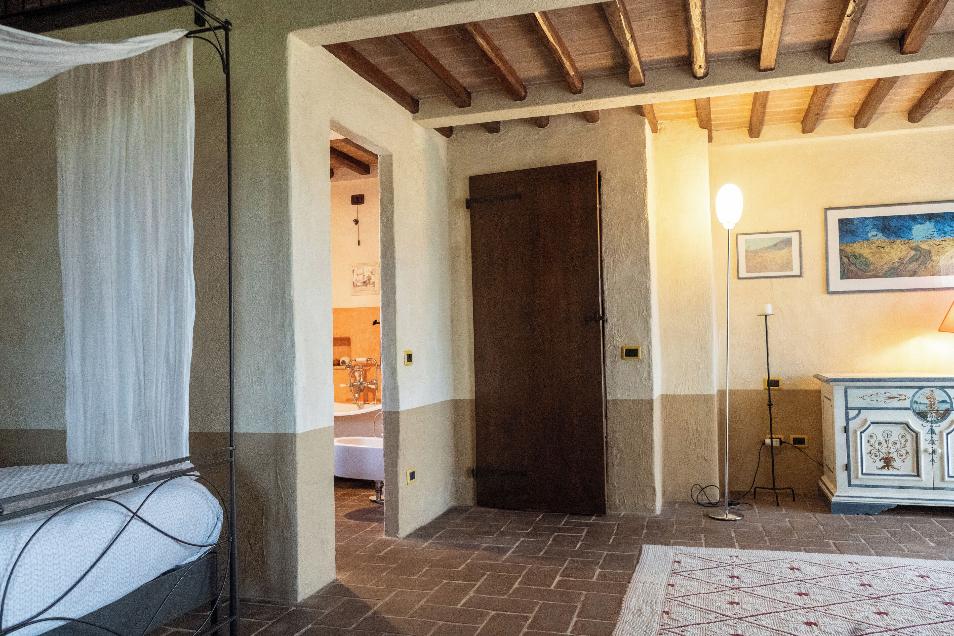 Un dormitorio con cama, una puerta de madera, una lámpara de pie y un cuadro en la pared.