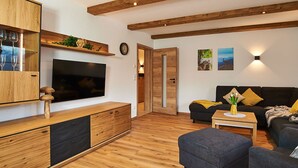 Un soggiorno moderno con pavimento in legno, TV a schermo piatto, divano, tavolino da caffè e pensile in legno.