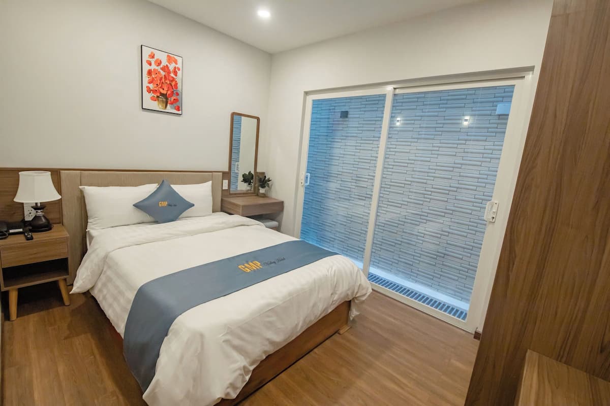 Hotelkamer met een bed, nachtkastje, lamp en een groot raam met uitzicht.