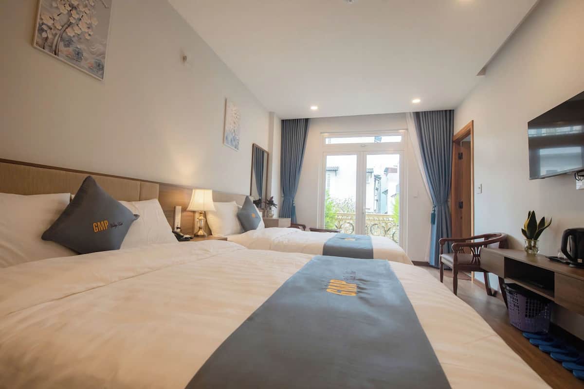 Een hotelkamer met twee bedden, een bureau, een stoel, een televisie en uitzicht op een balkon.