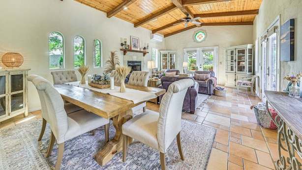 Un vaste espace de vie doté d’un plafond en bois, d’une table à manger avec des chaises et d’une cheminée.