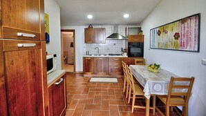 A kitchen with wooden cabinets, a tiled backsplash, a dining table with chairs, and a fruit bowl.