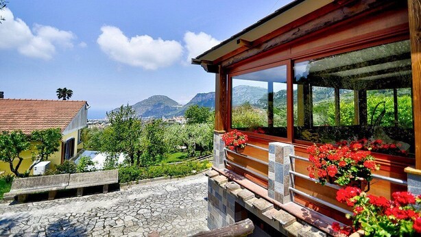 A building with a stone-paved courtyard, a wooden bench, and a window with red flowers.