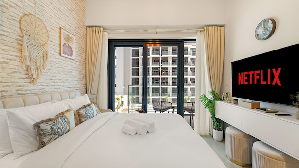 Habitación de hotel moderna con una cama grande, un televisor mostrando 'NETFLIX', un balcón con vistas a la ciudad y una pared decorada con un atrapasueños y un cuadro enmarcado.