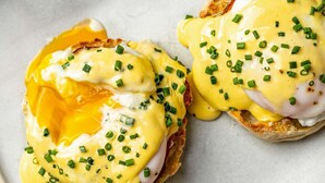 Twee gepocheerde eieren op muffins met hollandaisesaus en bieslook.