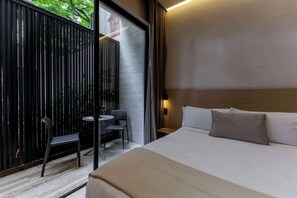 A hotel room with a bed, a small table, two chairs, a window, and a view of greenery outside.