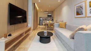 A modern living room with a flat-screen TV, a sofa, a coffee table, and a kitchen in the background. - Capitalia | Private Patio – Peaceful Polanco Stay (Ciudad de México)