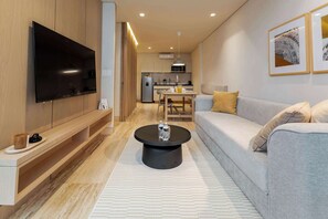 A modern living room with a flat-screen TV, a sofa, a coffee table, and a kitchen in the background.