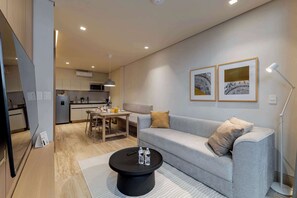 Un salon moderne avec un canapé gris, une table basse noire et un coin repas comprenant une table et des chaises en bois.