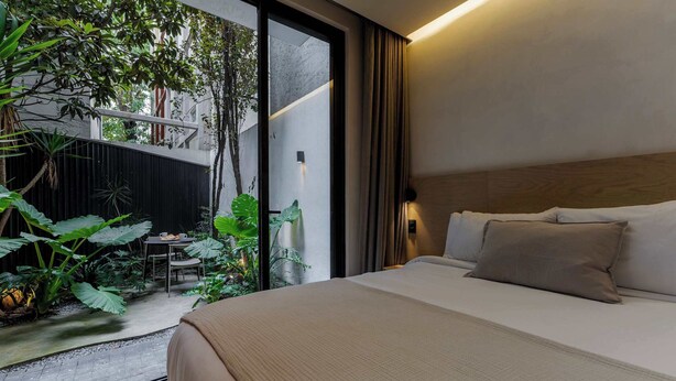 Een moderne hotelkamer met een groot bed, uitzicht op een tuin en een schuifdeur naar een buitenruimte.