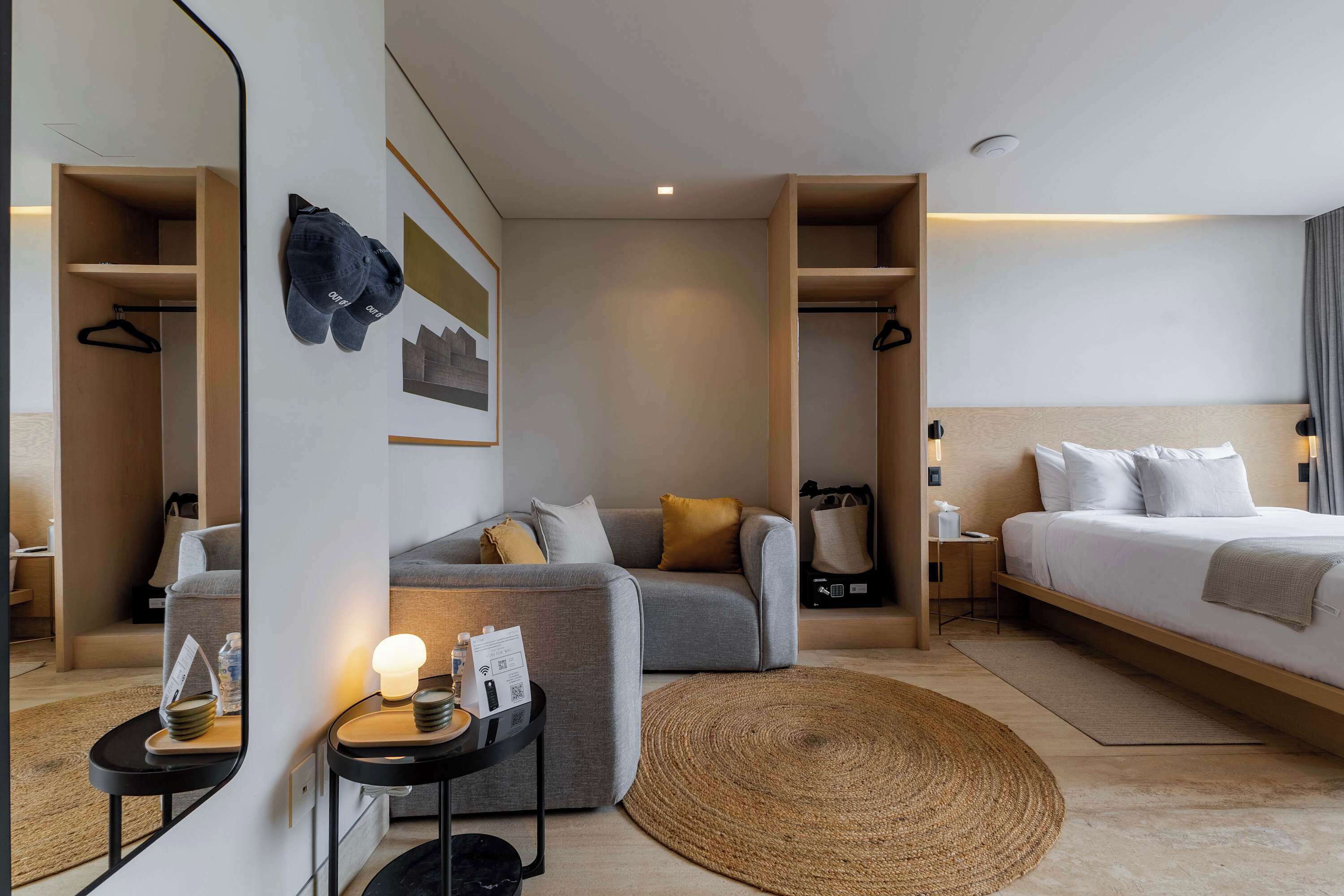 A modern hotel room with a bed, a sofa, a small table, a mirror, and a wardrobe.
