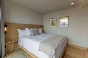 Un lit bien fait, avec une tête de lit en bois, une table de chevet avec une lampe et deux tableaux encadrés accrochés au mur.