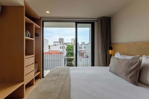 A hotel room with a bed, a wooden wardrobe, and a view of buildings through a glass door.
