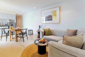 Un salon moderne avec un canapé, une table basse sur laquelle sont posés des croissants, un coin repas avec des chaises et, au fond, une cuisine.