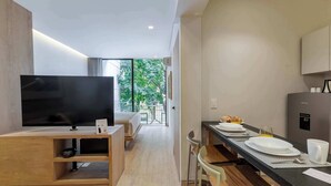 Ein modernes Hotelzimmer mit Fernseher, einem Essbereich mit Tisch für zwei Personen und einer Küchenzeile.