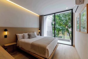 A modern bedroom with a large bed, bedside tables, a view of greenery through a sliding door, and a ceiling light.