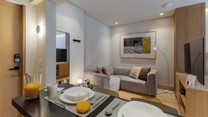 Ein modernes Hotelzimmer mit Essbereich, einer Couch, einem Fernseher und einem gerahmten Bild an der Wand.