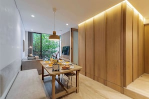 A modern dining area with a wooden table, bench seating, and a view of greenery outside.