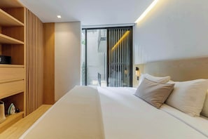 A modern hotel room with a large bed, wooden shelving, and a view through a sliding door.