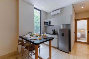 A modern kitchen with a dining table, chairs, a refrigerator, a microwave, and a window. - Capitalia | 1BR Chill Balcony Polanco Views & Wifi (Ciudad de México)