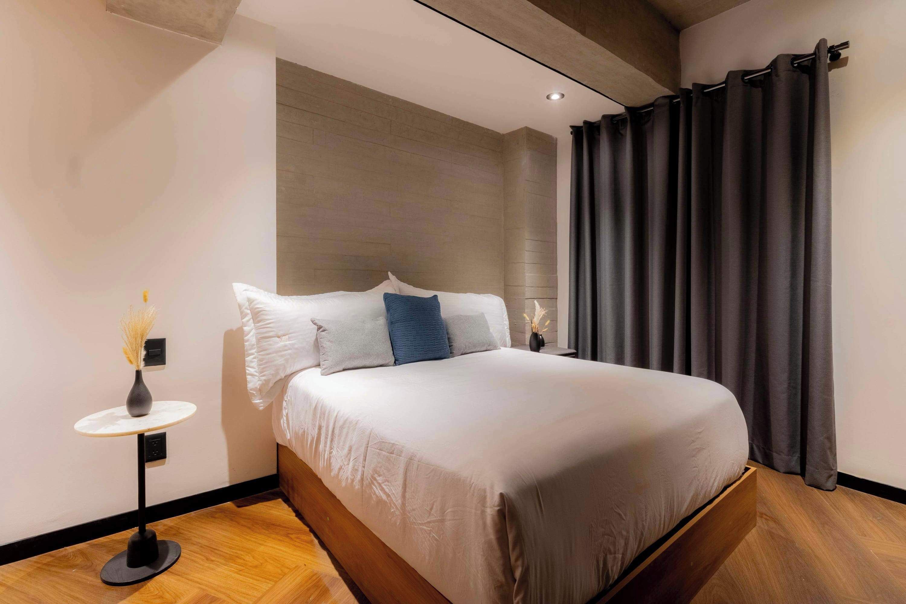 A modern bedroom with a large bed, a small bedside table, and a dark curtain.