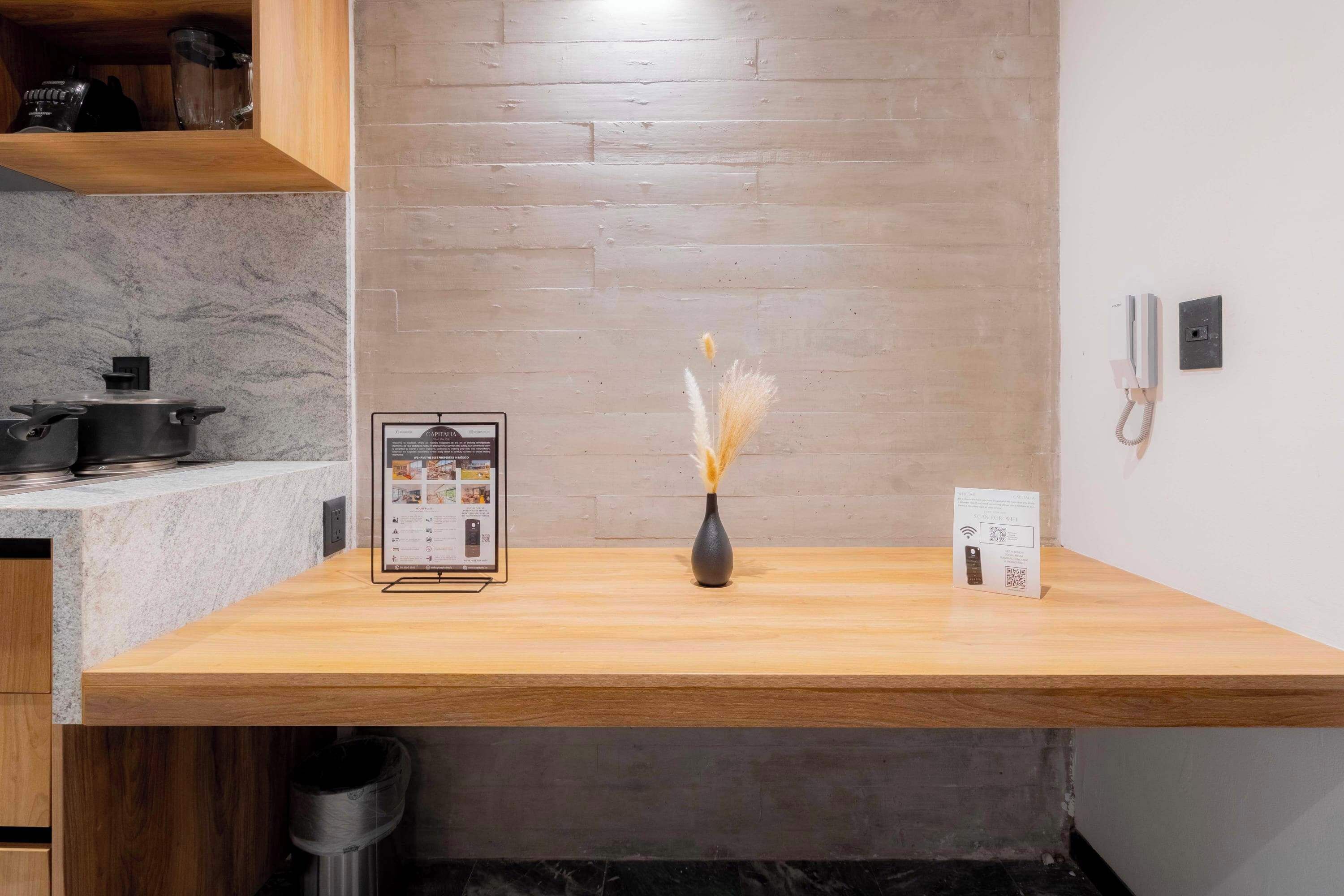 A kitchen counter with a vase of dried flowers, a digital menu board, and a phone on the wall.