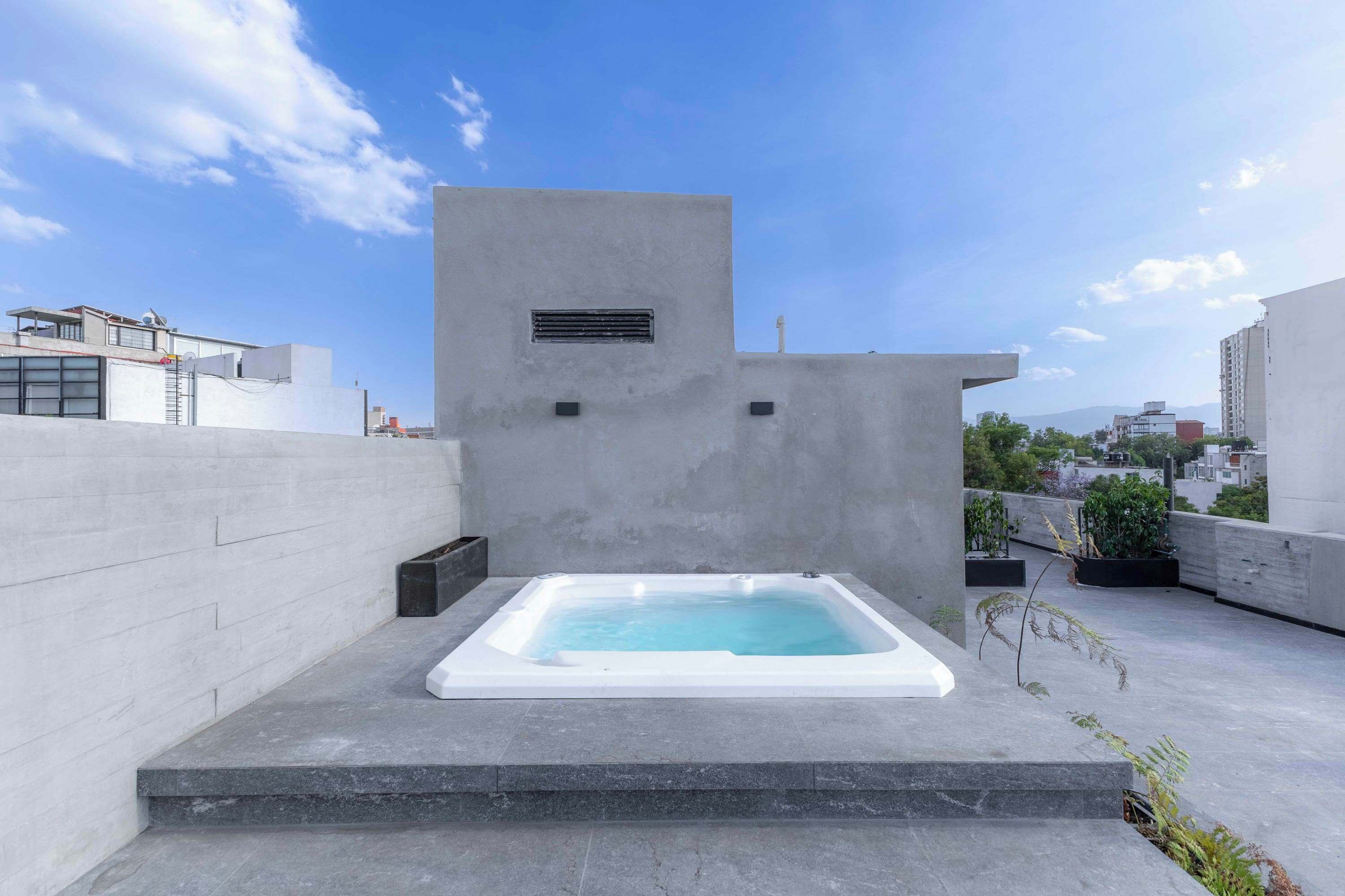 Une terrasse sur le toit avec un jacuzzi rectangulaire, un mur en béton et un ciel dégagé.