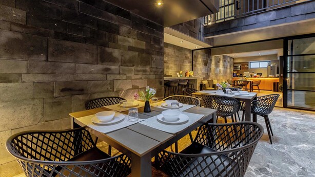 Un espace repas moderne avec un mur en pierre, des chaises en osier noir et une longue table dressée pour quatre personnes.