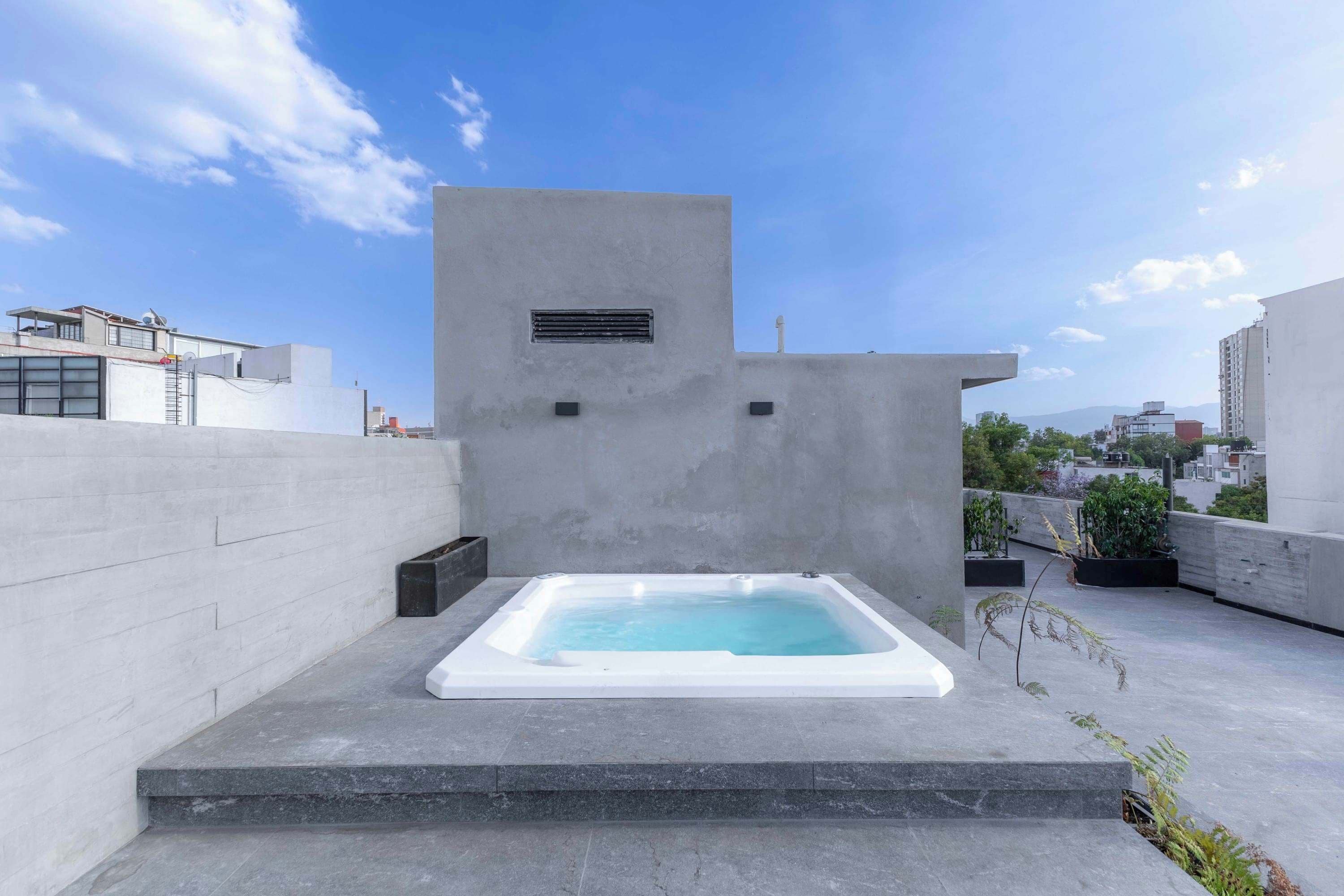 A rooftop with a rectangular hot tub, a concrete wall, and a clear sky.