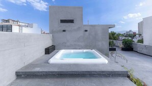 Une terrasse sur le toit avec un jacuzzi rectangulaire, un mur en béton et un ciel dégagé.