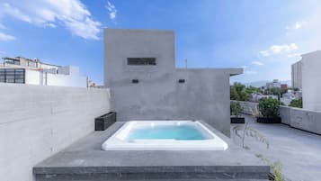 A rooftop with a rectangular hot tub, a concrete wall, and a clear sky.