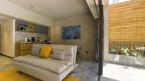 Un salon moderne comprenant un canapé, un coin cuisine et un balcon agrémenté de plantes.