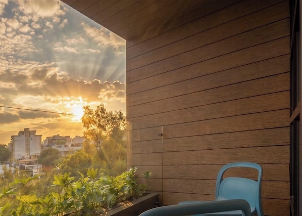 A balcony with a view of the sunset, wooden paneling, and a blue chair.