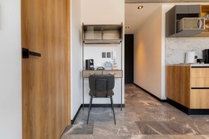A compact kitchenette with a microwave, coffee maker, and a small chair.