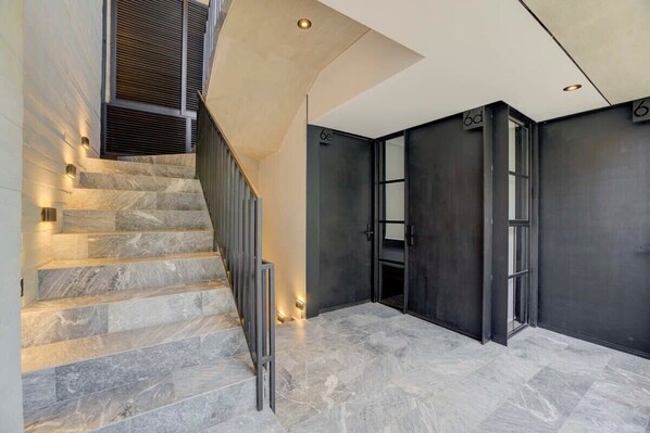 Um interior moderno com escadas de mármore, uma parede escura e uma porta com a inscrição '6d'.
