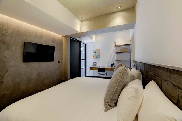 Une chambre d’hôtel moderne avec un grand lit, un téléviseur à écran plat fixé au mur et un bureau avec une chaise en arrière-plan.