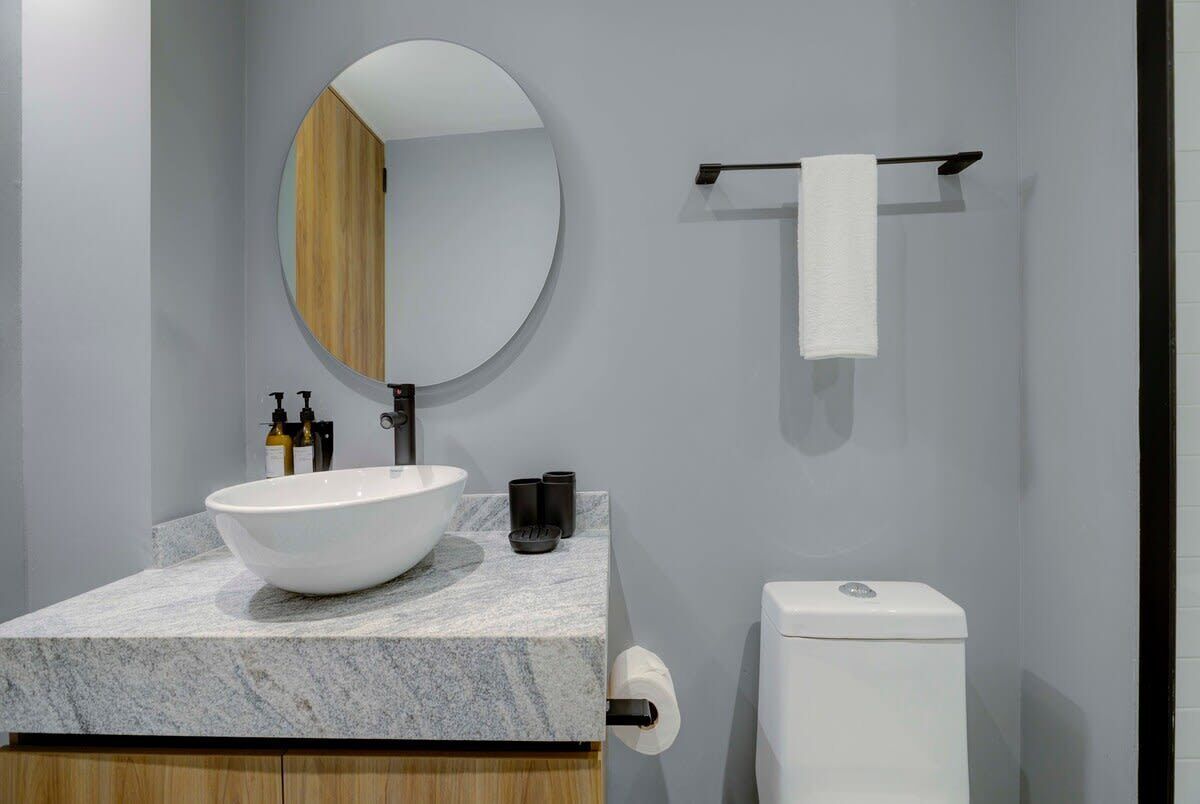 Een moderne badkamer met een ronde spiegel, een witte wastafel en een toilet.