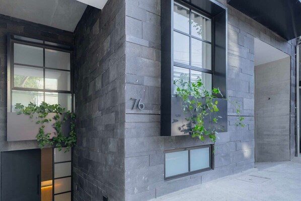 Un bâtiment moderne doté de grandes fenêtres, avec le chiffre « 76 » inscrit sur la façade, et des plantes vertes qui poussent sur les murs extérieurs.