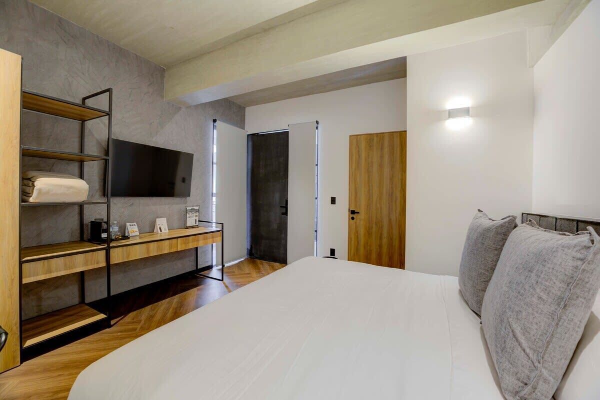 A modern bedroom with a large bed, a wooden shelf unit, a flat-screen TV, and a wardrobe.