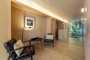A modern interior with wooden walls, a framed artwork, a reception desk, and a view of greenery outside.
