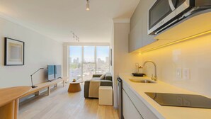 A modern kitchen with a built-in microwave, a sink, and a countertop. There is a bench and a small table in the living area with a view of the city. - Capitalia | Breezy A/C & Blazing-Fast Wi-Fi (Ciudad de México)