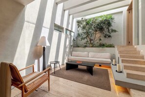 Ein modernes Wohnzimmer mit einer Couch, einem Couchtisch, einer Lampe, einer Bank und einer Treppe.