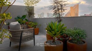 A rooftop terrace with wicker furniture, potted plants, and a view of city buildings. - Capitalia | Breezy A/C & Blazing-Fast Wi-Fi (Ciudad de México)