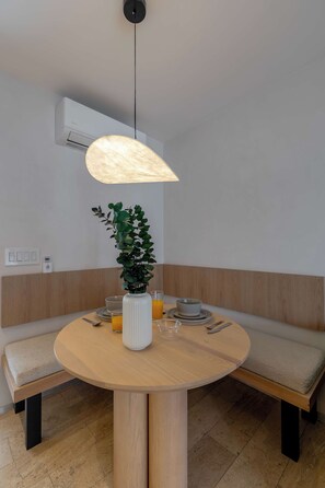 A round dining table with a white vase and a potted plant, surrounded by wooden benches.