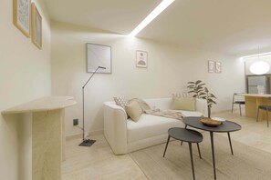 A living room with a white sofa, a small round table with a bowl, a floor lamp, and a potted plant.