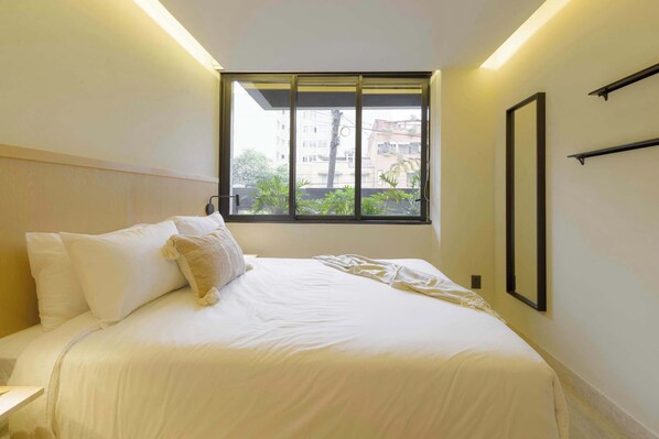 A hotel room with a bed, a window, and a wall-mounted shelf.