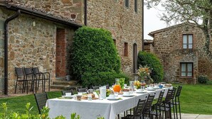 An outdoor dining area with a table set for breakfast, surrounded by stone buildings and greenery. - Villa Saffo: A charming three-story villa surrounded by meadows and by green hills, with Free WI-FI. (Bucine)